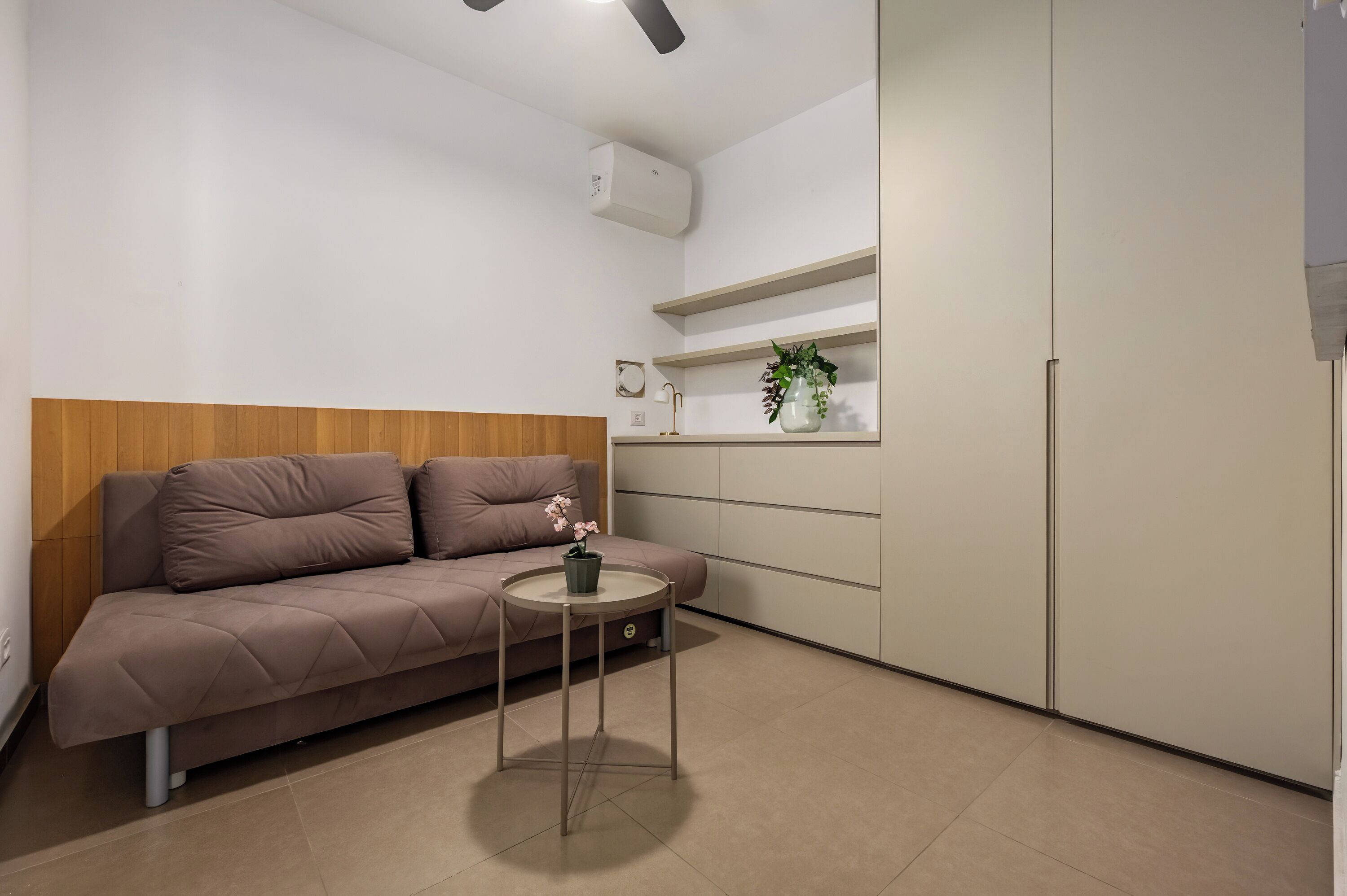 A modern living room with a sofa, a small round table with a plant, and built-in shelving.