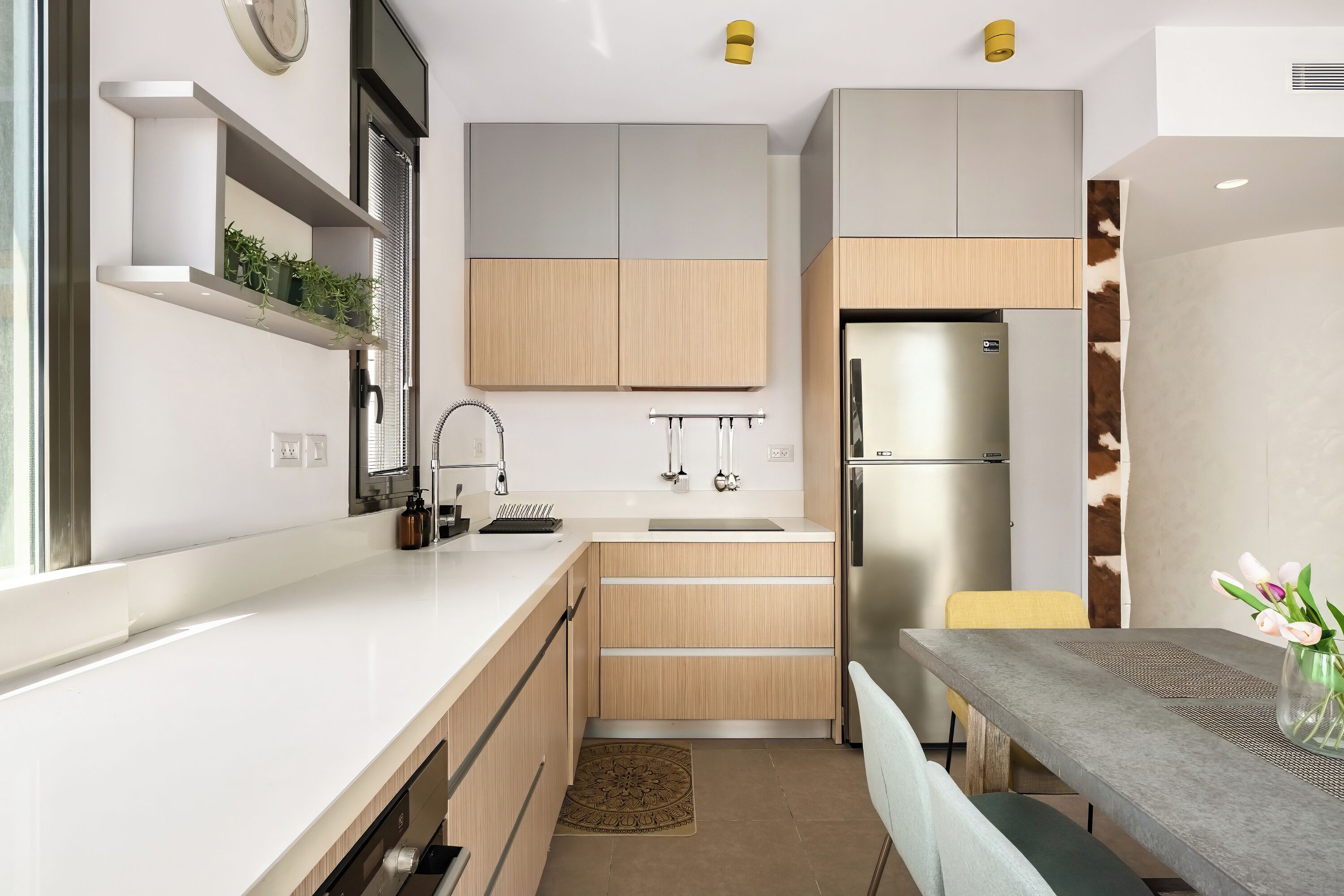 A modern kitchen with white countertops, wooden cabinets, and a stainless steel refrigerator.
