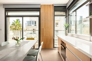 Une cuisine moderne dotée d’une grande fenêtre, un coin repas avec une table et des chaises, et une vue sur le paysage urbain.