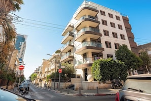 Un immeuble résidentiel à plusieurs étages, doté de balcons, d’un panneau indiquant l’interdiction d’accès et d’une voiture garée.