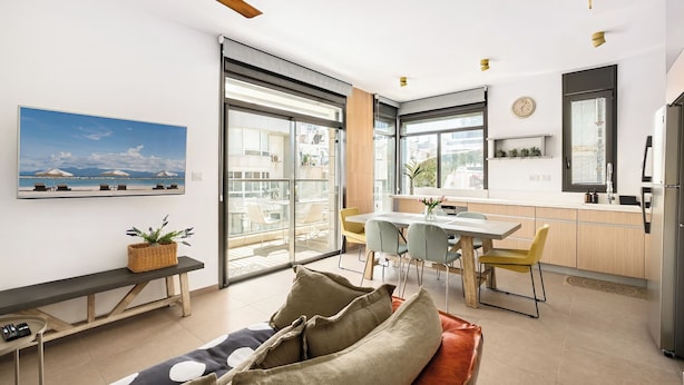 A modern kitchen with a dining area, large windows, and a ceiling fan. - Sea Breeze – Luxury 3BR Beachfront Apartment on Zrubavel Street (Tel Aviv-Yafo)