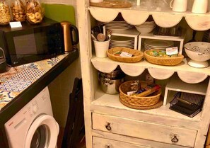 Eine Küche mit Waschmaschine, Mikrowelle und Regalen, ausgestattet mit Körben und Geschirr.