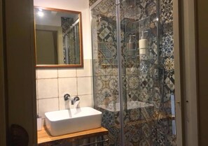 Ein Badezimmer mit einem weißen Waschbecken, einem Spiegel und einer Dusche mit gemusterten Fliesen.