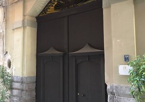 Eine große, dunkle Holztür mit dekorativer Oberseite, eingebaut in ein Gebäude mit einer beigen Wand und einem Steinsockel.