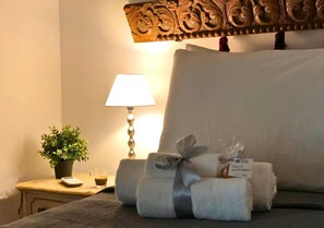 Ein ordentlich bezogenes Bett mit Kissen, einer Nachttischlampe, einem kleinen Tisch mit Pflanze und Tasse sowie einer Willkommenskarte.