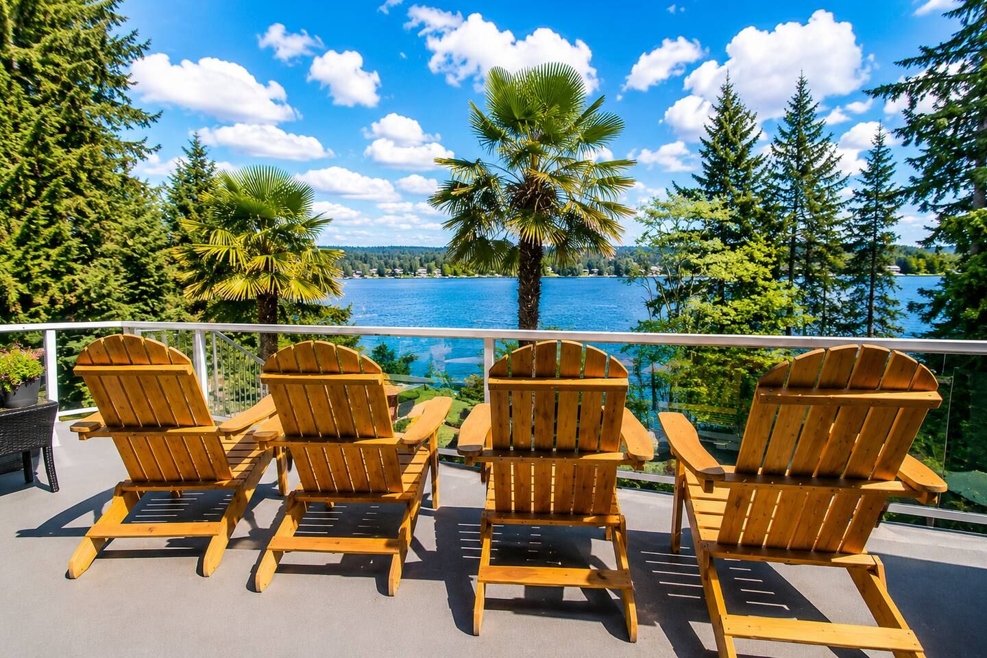 A deck with four wooden Adirondack chairs facing a body of water, surrounded by trees and a clear sky.