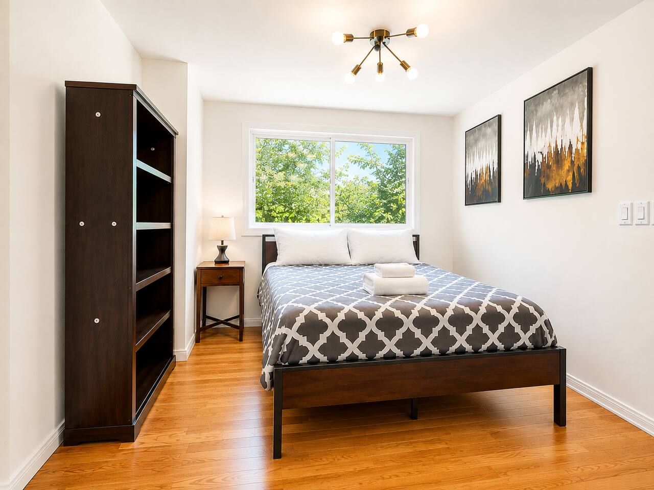 A bedroom with a bed, a wardrobe, a nightstand, and a window with a view of trees.