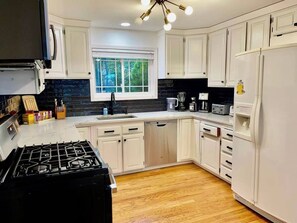 A modern kitchen with white cabinets, a black stove, and a window above the sink.
