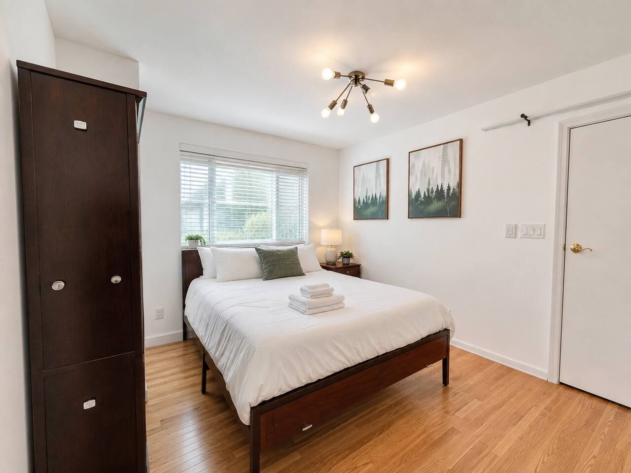 A bedroom with a bed, a wardrobe, a nightstand, a lamp, and two framed pictures on the wall.