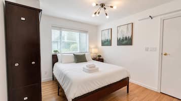 A bedroom with a bed, a wardrobe, a nightstand, a lamp, and two framed pictures on the wall.
