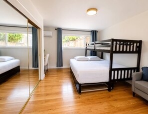 A room with a bunk bed, a single bed, a sofa, a chair, and a large window with curtains.