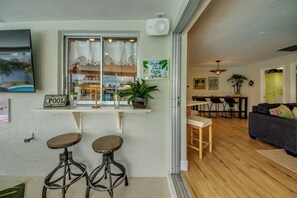 A cozy living area with a dining table, two bar stools, a sofa, and a window with a view. - Hibiscus Hideaway – Tropical Waterfront Paradise Villa 26 (Cape Coral)