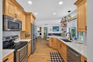A modern kitchen with wooden cabinets, stainless steel appliances, and a checkered floor. - Hibiscus Hideaway – Tropical Waterfront Paradise Villa 26 (Cape Coral)