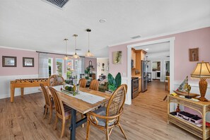 A spacious dining area with a wooden table and chairs, a kitchen in the background, and a view of the outdoors. - Hibiscus Hideaway – Tropical Waterfront Paradise Villa 26 (Cape Coral)