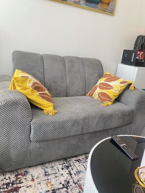 Ein graues Sofa mit gelb-braunen Kissen, einer Fernbedienung und einem schwarzen Couchtisch mit weißem Rand.
