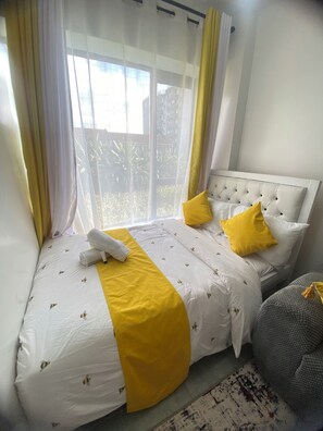 Ein Schlafzimmer mit einem Bett, einem Fenster mit Vorhängen und Blick auf Grün.