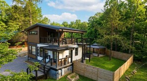 A modern two-story house with a deck, surrounded by a wooden fence and lush greenery.