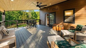 Eine überdachte Terrasse mit Sitzgelegenheiten, einem Deckenventilator und Blick auf den umliegenden Wald.
