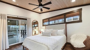 Ein Schlafzimmer mit einem großen Bett, einem Deckenventilator, einer Schiebetür zu einem Balkon und Blick ins Freie.