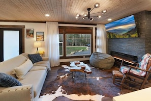 A cozy living room with a sofa, a coffee table, a fireplace, and a large window with a view of the outdoors. - New- Hot tub, firepit, fenced-in yard, near the Smoky Mountain National Park! (Gatlinburg)