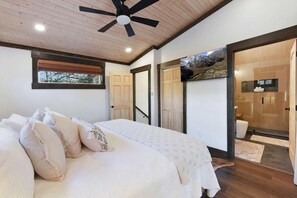 A bedroom with a bed, pillows, a ceiling fan, a window, and a door leading to a bathroom. - New- Hot tub, firepit, fenced-in yard, near the Smoky Mountain National Park! (Gatlinburg)
