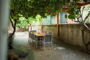 An outdoor patio with a wooden table and chairs, surrounded by a brick floor and a concrete wall. - Bike Lodge Finalborgo (Finale Ligure)