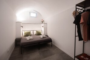 A bedroom with a bed, a nightstand, a wall-mounted shelf with clothes, and a small window. - Bike Lodge Finalborgo (Finale Ligure)
