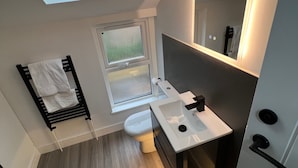 A modern bathroom with a skylight, a toilet, a sink, and a towel rack. - House Sleeps 6 With Enclosed Garden (Cardiff)