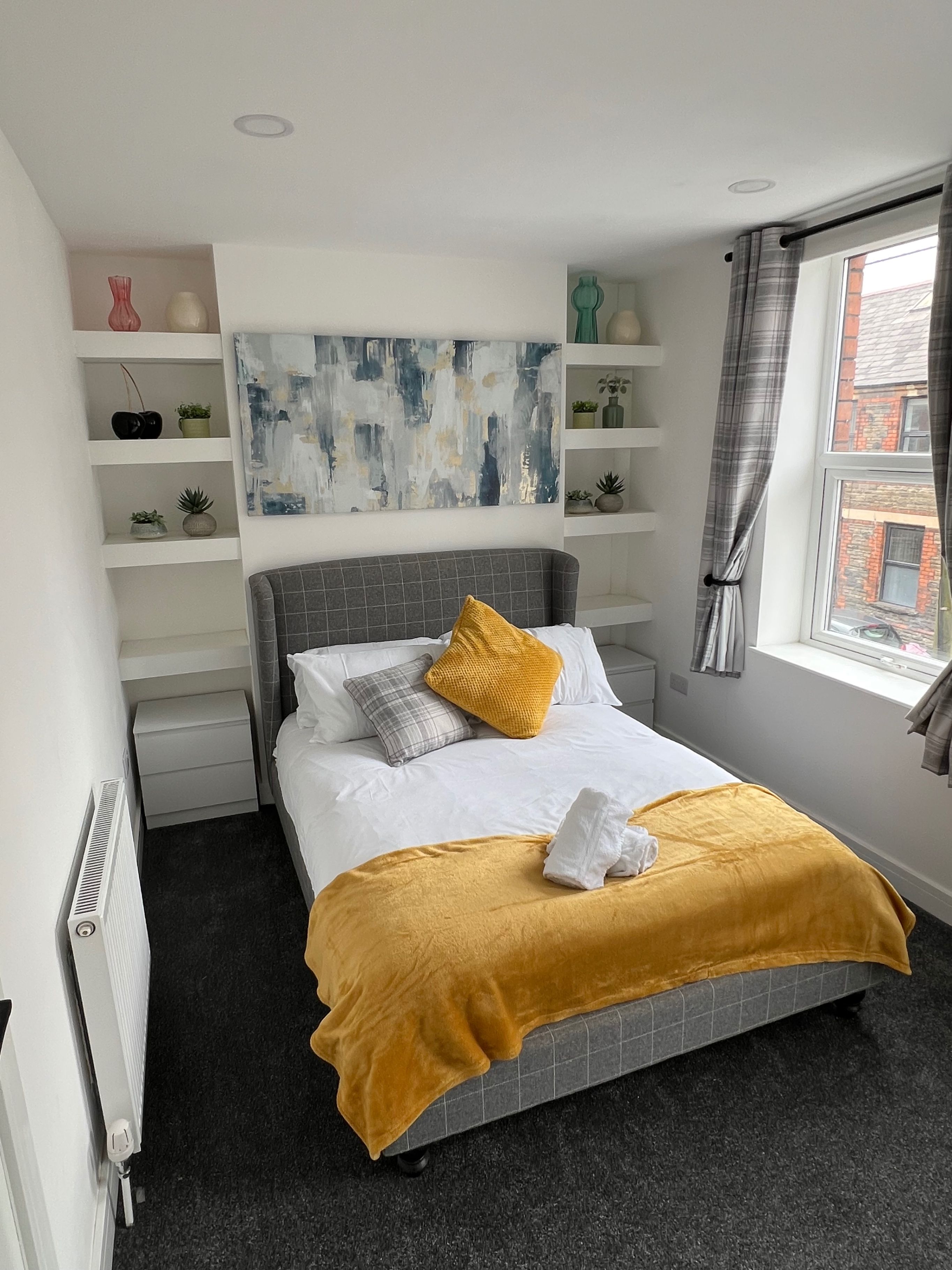 A modern bedroom with a bed, a radiator, a window with curtains, and a wall with shelves.