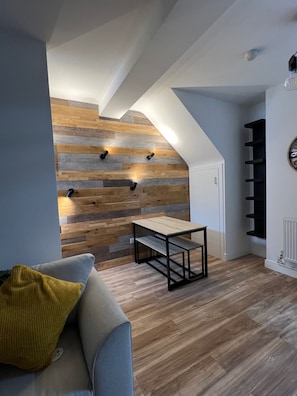 Un interior moderno con techo inclinado, pared de madera con iluminación empotrada, una pequeña mesa y un sofá con un cojín amarillo.
