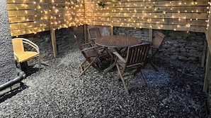 A patio area with a wooden table and chairs, surrounded by a wooden fence adorned with string lights. - House Sleeps 6 With Enclosed Garden (Cardiff)