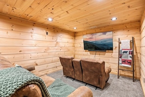 Interior d'una cabana de fusta amb un sofà, una televisió i un quadre d'un paisatge de muntanya.