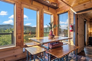 A wooden interior with a table and benches, large windows, and a view of a forested mountain. - Thunder Bear Ridge | Mountain Views & Hot Tub (Sevierville)