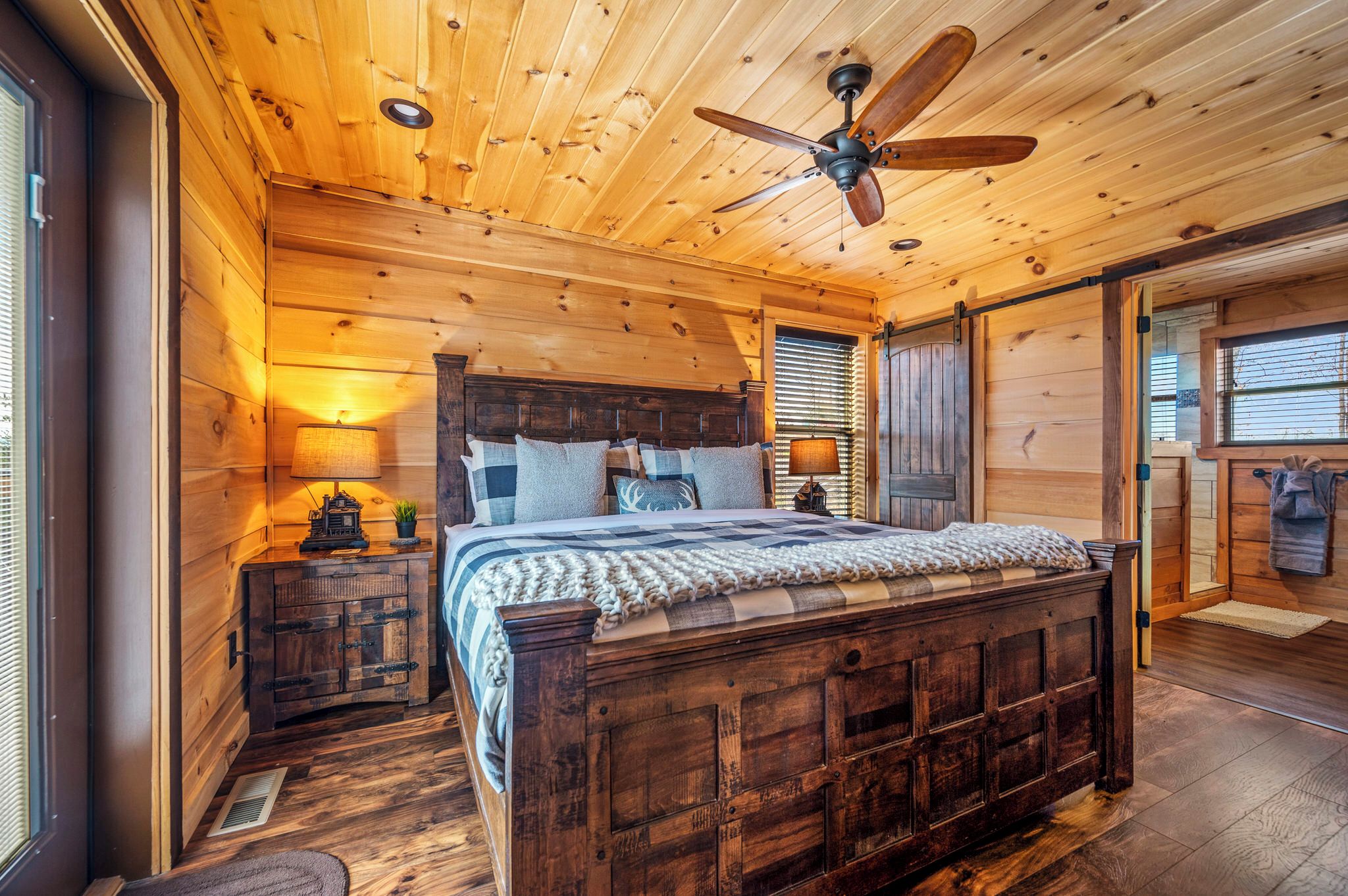Une chambre à coucher en bois, avec un lit, un ventilateur de plafond et une table de chevet avec une lampe.