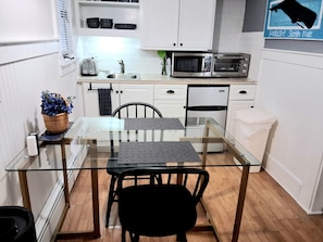 A compact kitchen with a glass dining table, black chairs, white cabinets, a microwave, and a toaster.