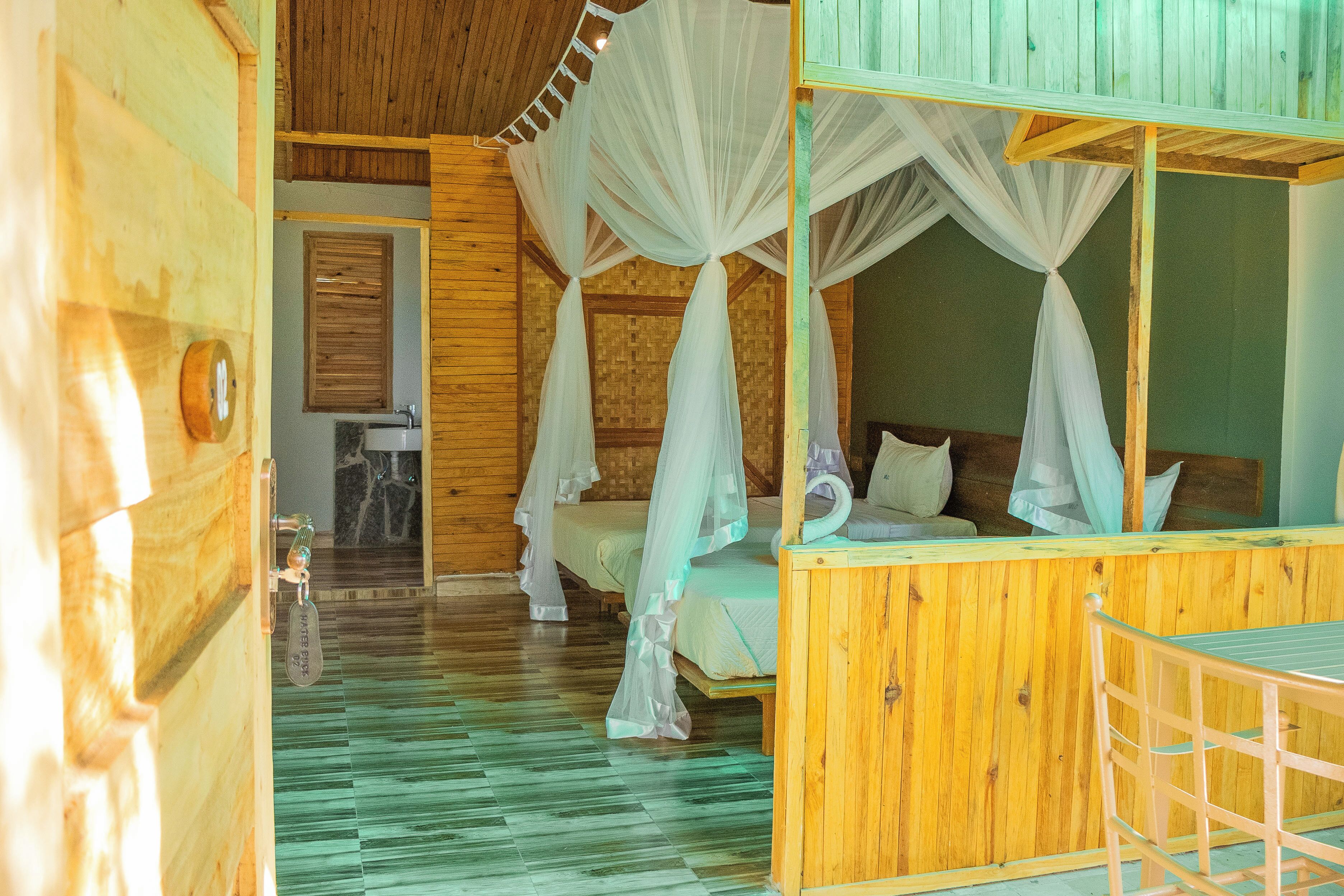 A wooden cabin with a bed under a canopy, a small bathroom, and a wooden floor.