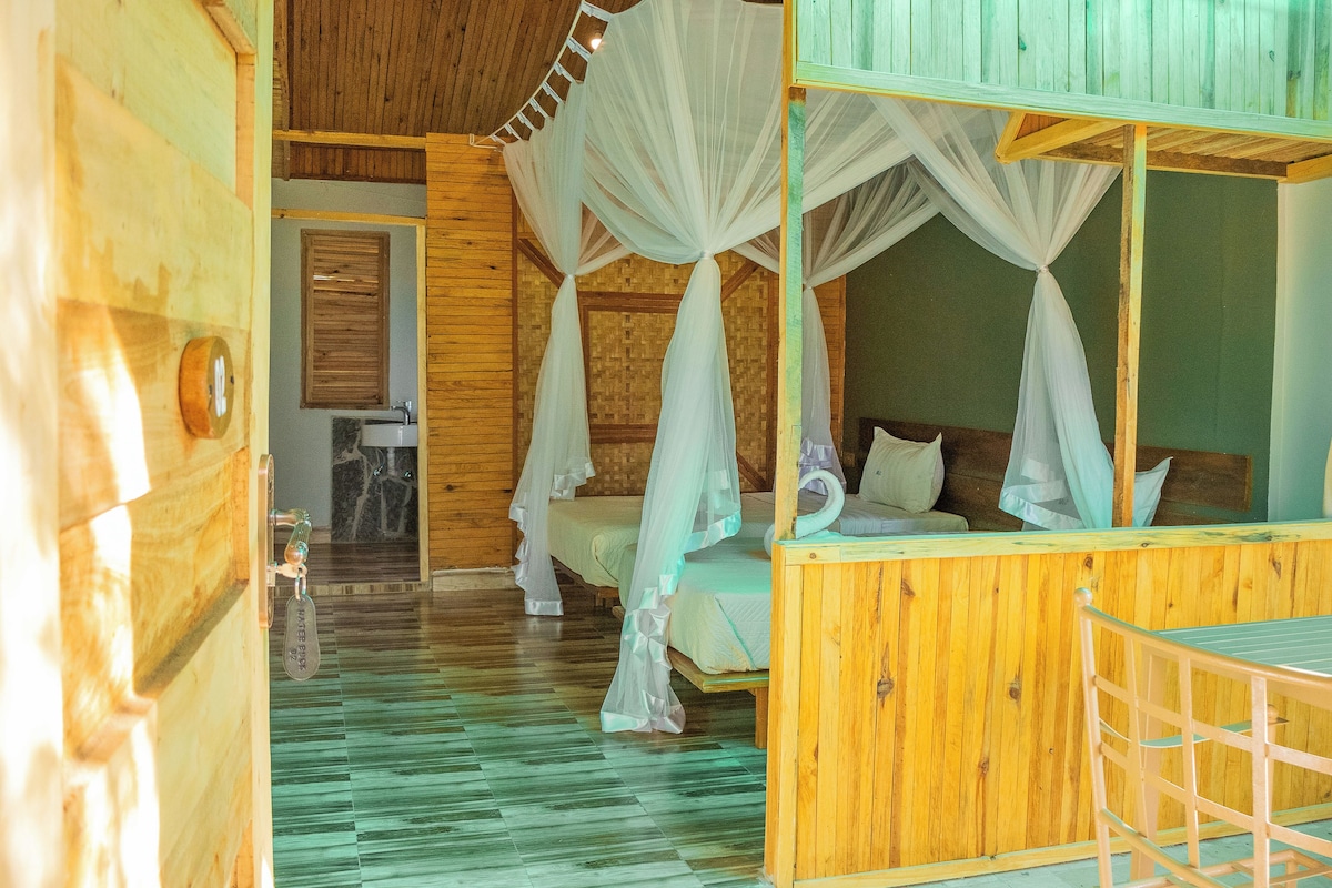 A wooden cabin with a bed under a canopy, a small bathroom, and a wooden floor.
