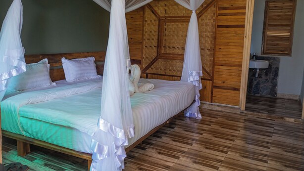 A room with a four-poster canopy bed, wooden flooring, and a visible bathroom with a sink. - Basecamp Resort Mweya (Mweya)