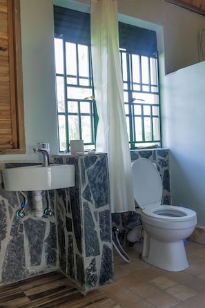 A bathroom with a stone sink, a toilet, and a window with a curtain. - Basecamp Resort Mweya (Mweya)