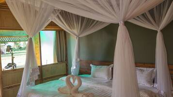 A four-poster bed with a canopy, a wooden headboard, and two swan-shaped towels.
