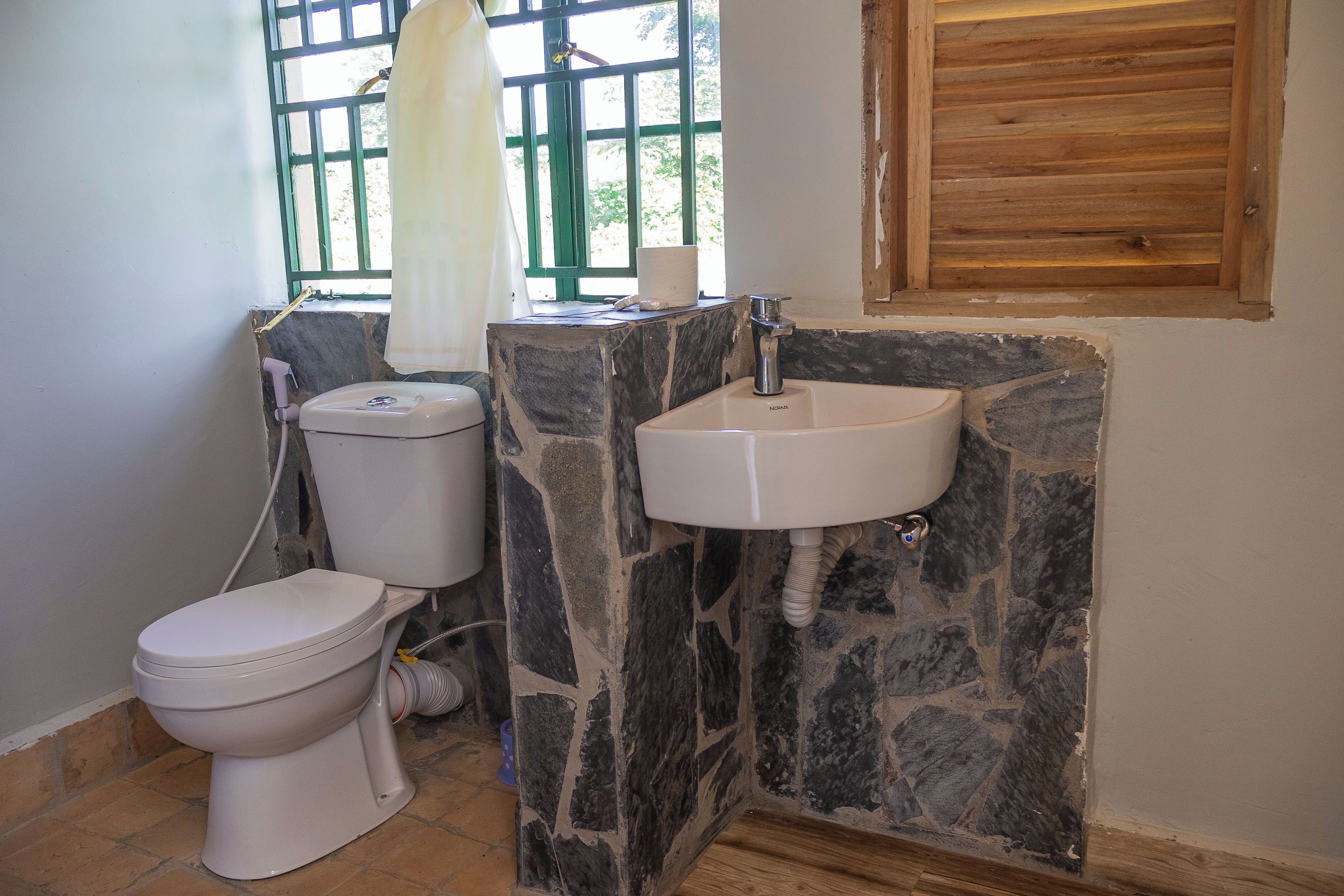 A bathroom with a toilet, a sink, and a window with a view of greenery.