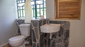 A bathroom with a toilet, a sink, and a window with a view of greenery. - Basecamp Resort Mweya (Mweya)