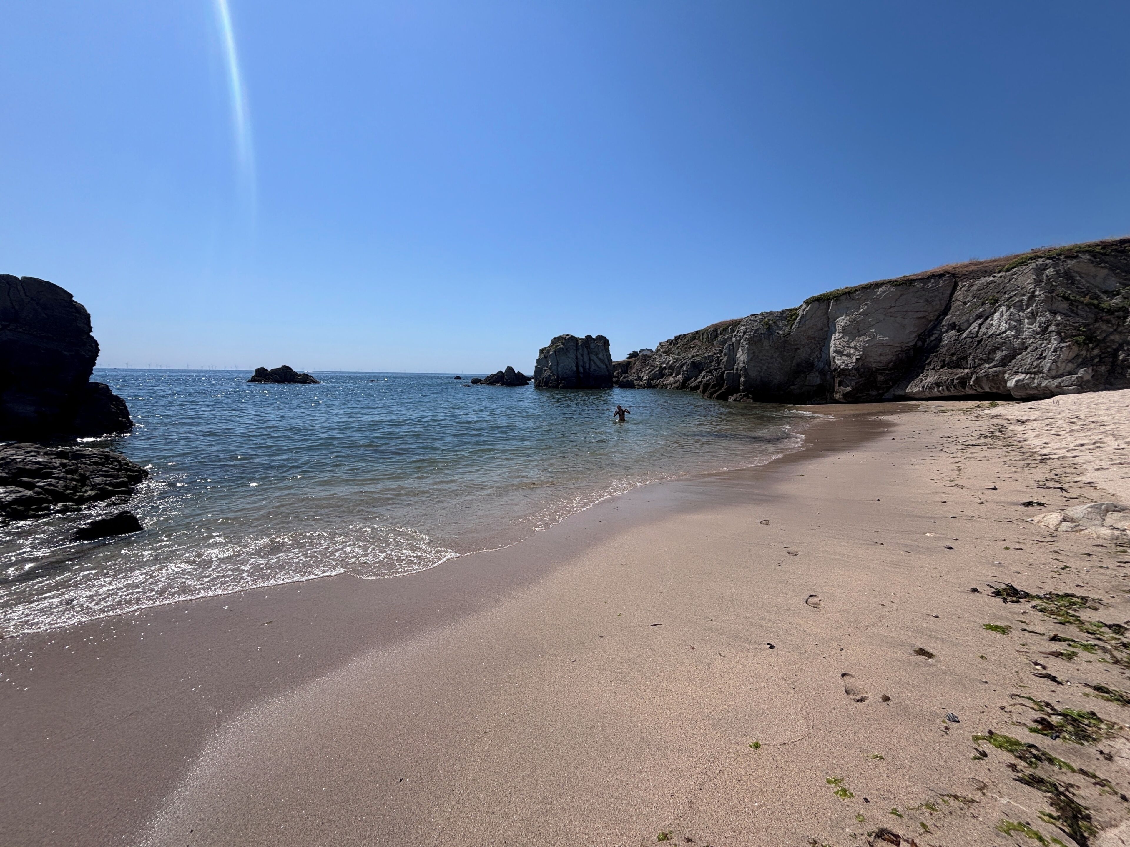 Uma praia com águas cristalinas, falésias rochosas e uma pessoa na água.