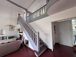 A staircase with a white railing leading to a landing, a sofa with cushions, and a hanging light fixture. - Maison 14 personnes côte sauvage Le Pouliguen / House for 14 people Le Pouliguen (Le Pouliguen)