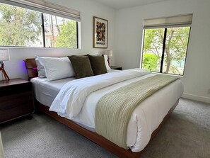 A bedroom with a large bed, two bedside tables, a lamp, and a framed picture on the wall. - Riviera Palms - A Ryson Property (Palm Springs)