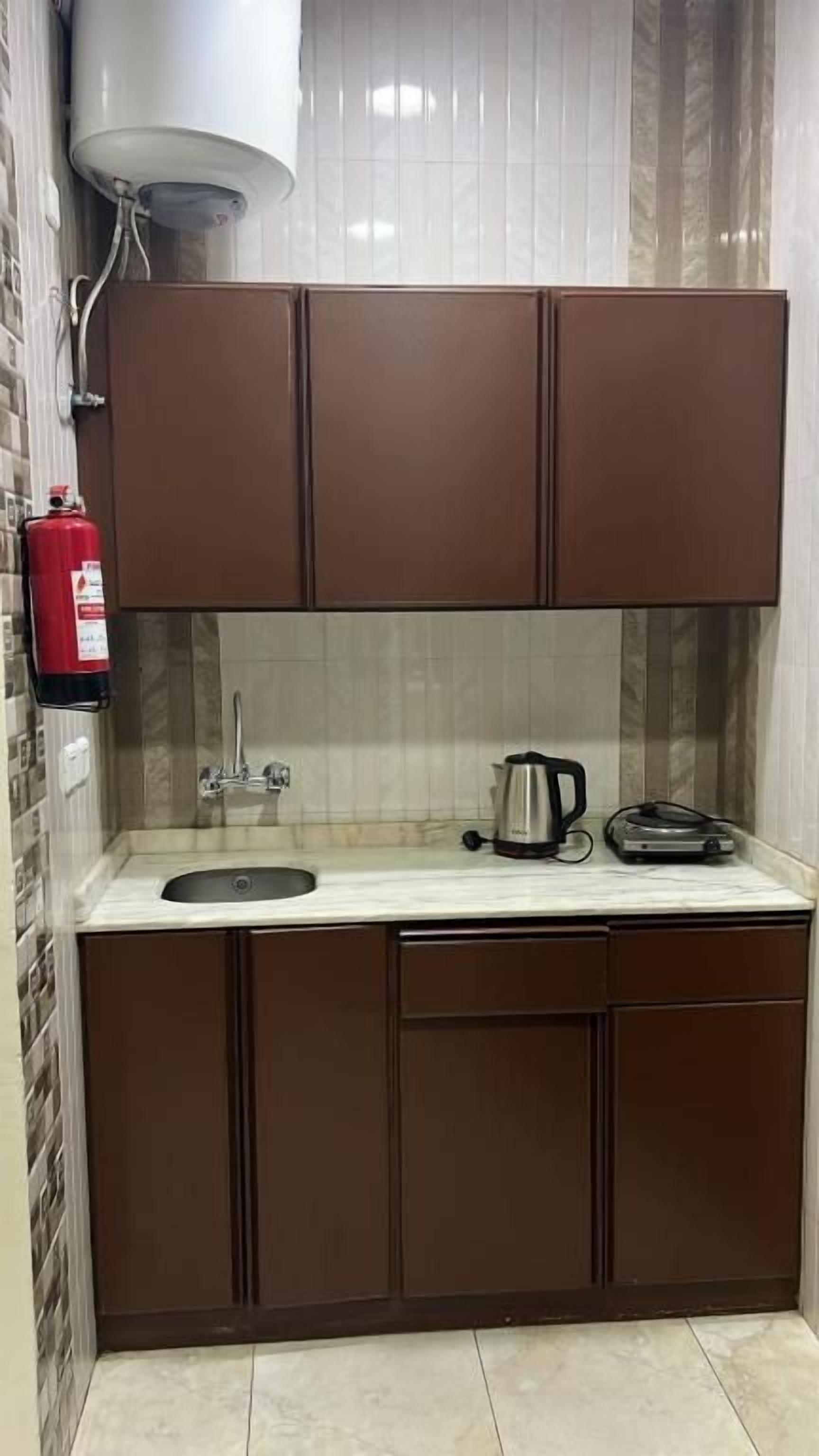 Una cocina compacta con un lavamanos, una tetera y un tostador sobre la encimera.