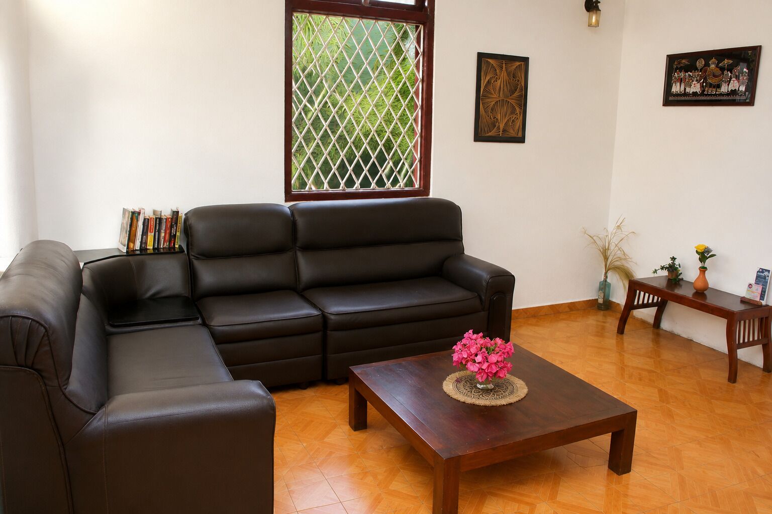 Una sala de estar con un sofá de cuero negro, una mesa de centro de madera con un florero, una mesita con un florero y una planta, y una pared decorada con obras enmarcadas.