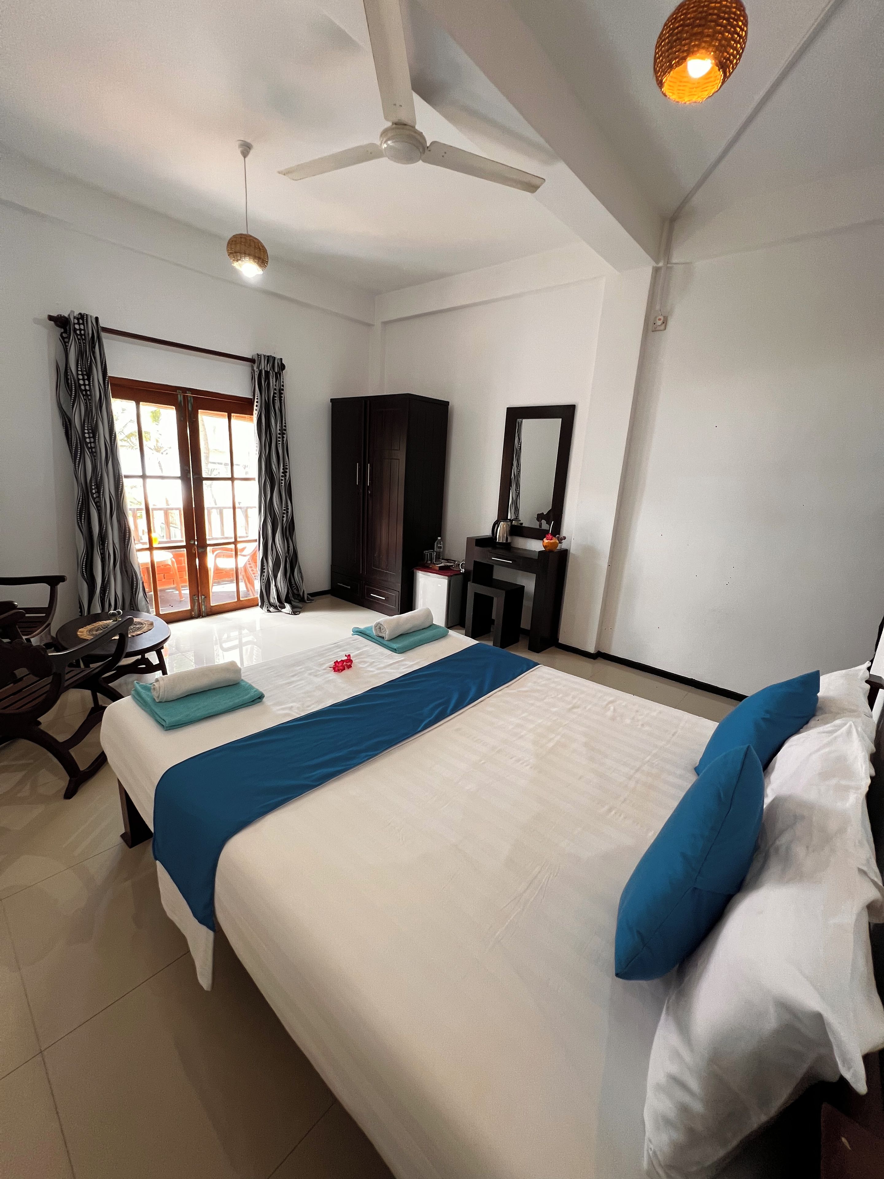A hotel room with a bed, a desk, a chair, a wardrobe, and a ceiling fan.