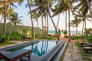 A pool area with lounge chairs and a view of the beach and ocean.