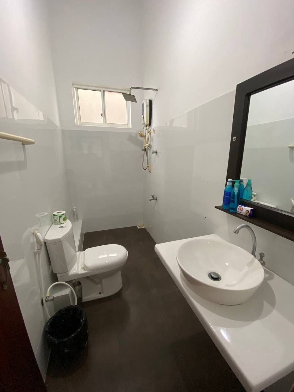 A bathroom with a toilet, sink, shower, and a window.